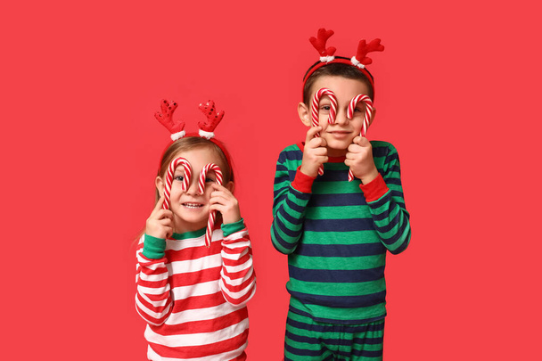 Αστεία μικρά παιδιά με πιτζάμες με καραμέλες σε κόκκινο φόντο - Φωτογραφία, εικόνα