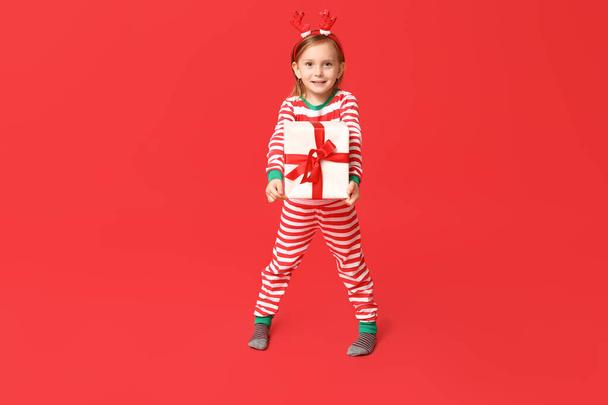 Linda niña en pijama con regalo de Navidad sobre fondo rojo - Foto, Imagen