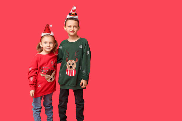 Leuke kleine kinderen in Kerst truien op rode achtergrond - Foto, afbeelding