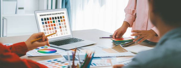 Portret kreatywnego zespołu grafików dobierają odpowiedni kolor dla projektu za pomocą laptopa na stole ze sprzętem i projektowanie narzędzia rozrzucone wokół w nowoczesnym biurze. Zbliżenie. Różnorodność. - Zdjęcie, obraz