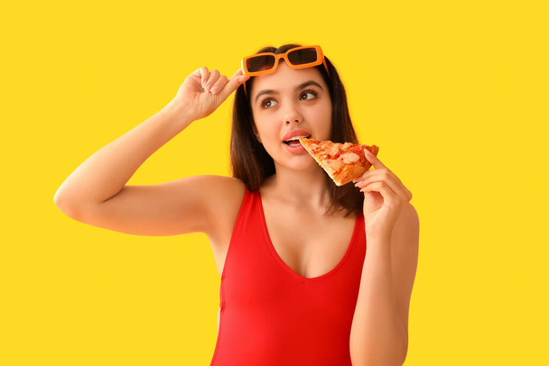 黄色い背景に美味しいピザを食べている若い女性 - 写真・画像