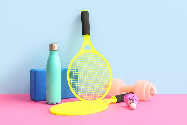 Tennis rackets with sports bottle and dumbbell on colorful background - Photo, Image
