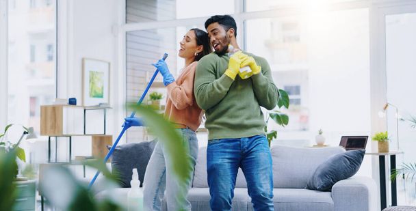 Ευτυχισμένο ζευγάρι, χορεύοντας και τραγουδώντας ενώ καθαρίζετε το σαλόνι μαζί για διασκέδαση απολύμανσης ή υγιεινής στο σπίτι. Άνδρες και γυναίκες που απολαμβάνουν την καθαριότητα, τα μικρόβια και τα βακτήρια απομάκρυνση στο σαλόνι στο σπίτι. - Φωτογραφία, εικόνα