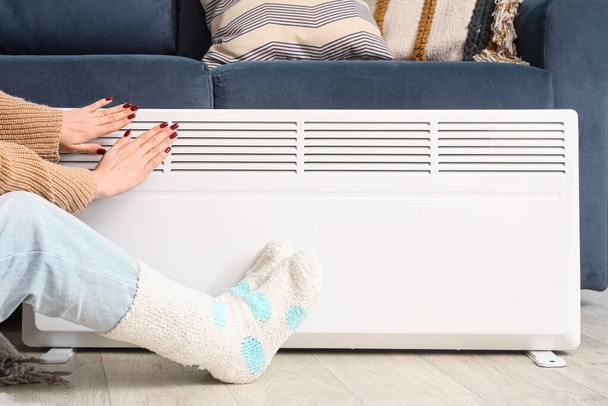 Nainen lämpimissä sukissa lähellä sähkölämmitintä kotona. Lämmityskauden käsite - Valokuva, kuva