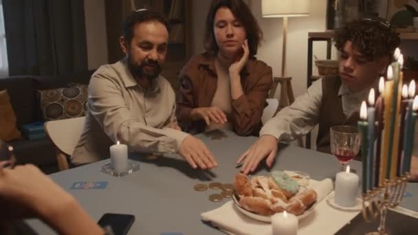 Tiro médio de homem judeu de meia-idade em kippah sentado à mesa com seus filhos em Hanukkah, girando dreidel, apostando com moedas de chocolate gelt, recebendo carta hebraica Nun, o que significa nada - Filmagem, Vídeo