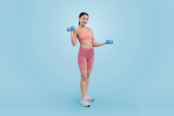 Vigorous energetic woman doing dumbbell weight lifting exercise on isolated background. Young athletic asian woman strength and endurance training session as body workout routine. - Photo, Image