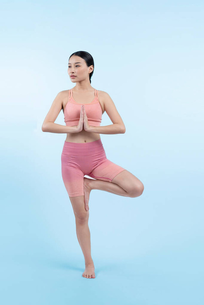 Azjatka w odzieży sportowej ćwiczy jogę w pozycji stojącej na siłowni jako rutyna treningowa. Zdrowa pielęgnacja ciała i medytacja jogi stylu życia w pełnym ujęciu na odosobnionym tle. Energiczny - Zdjęcie, obraz