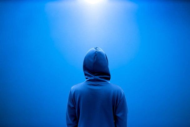 Abstract A Man in hood stand behind on blue background with space for text or graphic design. back view look like a hacker man. - Photo, Image