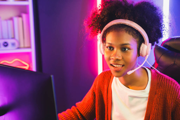 Африканська американська дівчина стример грає в онлайн-бої з досвідченою командою Esport в навушниках в неоновому кольоровому освітленні. Говорячи про інших гравців, які планують стратегії, щоб виграти конкурентів. Смаколик. - Фото, зображення