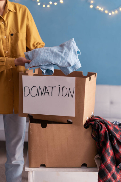 Концепція пожертвування. Жінка кладе одяг в коробку пожертвувань вдома. Крупним планом - Фото, зображення