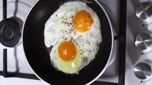 Deux œufs de poulet sont frits dans une casserole en gros plan au ralenti. Concept de petit déjeuner. Images verticales. - Séquence, vidéo