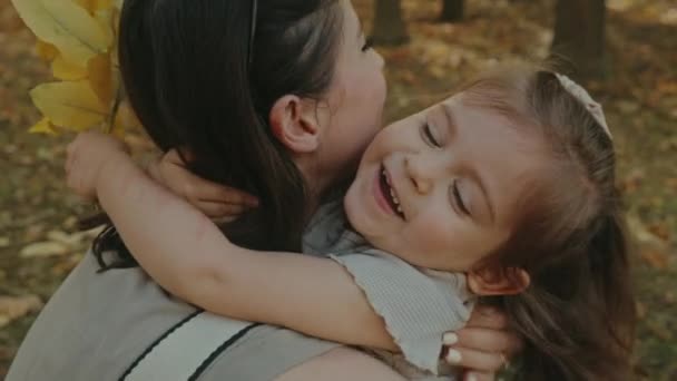 Daughter hugging tightly her mother, having fun in autumn park. Family spending time together at sunset on vacation. Concept of autumn holiday. - Footage, Video