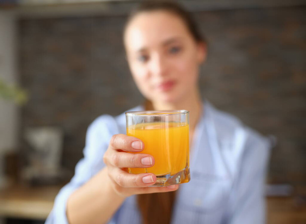 junges attraktives Mädchen im Schlafanzug in der Küche, das Orangensaft trinkt und ein Glas in der Hand hält - Foto, Bild