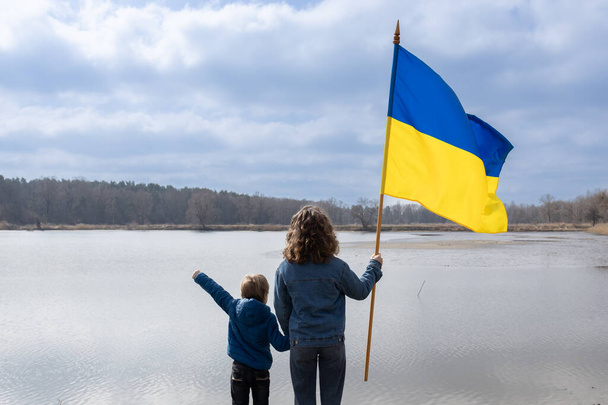 chlapec a mladá žena, mladší bratr a dospělá sestra, stojí vedle sebe a drží se za ruce s velkou vlajkou Ukrajiny. Zadní pohled. Rodina, jednota, uprchlíci, podpora. den důstojnosti a svobody - Fotografie, Obrázek