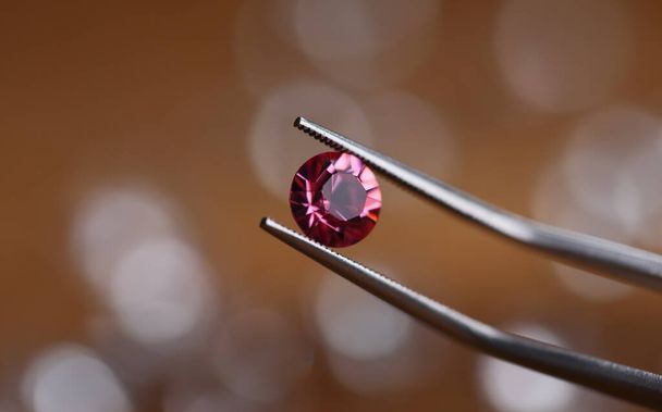Juwelier in werkplaats houdt roze steen in pincet klem close-up. Edelstenen verwerkingsconcept - Foto, afbeelding