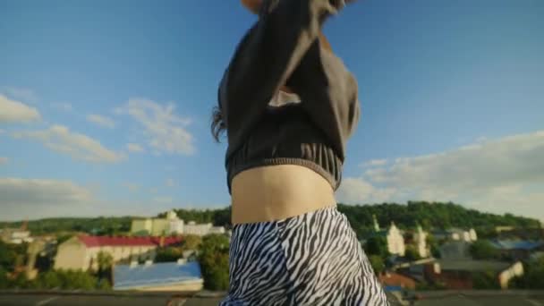 Talentuosa artista hip-hop femminile mette in mostra movimenti dinamici di danza su un tetto, affascinando la fotocamera con gesti cool. Spettacolo di street dance in ambiente urbano - Filmati, video