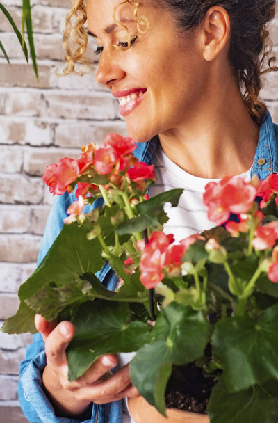 Πορτρέτο της ευτυχούς γυναίκας κρατώντας λουλούδια και το φυτό στο σπίτι σε ένα τοίχο φόντο τούβλο. Οι γυναίκες χαμογελούν αφού λάβουν ένα φυσικό δώρο. Επέτειος και γενέθλια έννοια παρόντες - Φωτογραφία, εικόνα