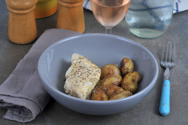 Φιλέτο μπακαλιάρου σε σάλτσα μουστάρδας με πατάτες σερβιρισμένες σε πιάτο με πιρούνι και ένα ποτήρι κρασί - Φωτογραφία, εικόνα