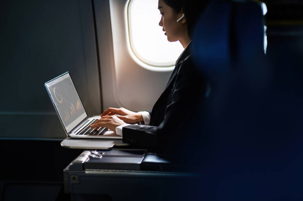 Успешная азиатская бизнес-леди, деловая женщина, работающая в салоне самолета во время полета на ноутбуке. - Фото, изображение
