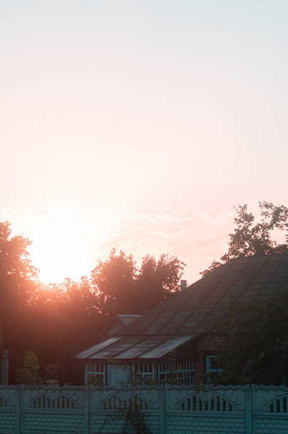 Morgens in der ländlichen Ukraine wärmt das zarte Glühen der Morgendämmerung ein charmantes Ferienhaus, und der Sonnenaufgang weckt sanft die Essenz des ruhigen Dorflebens - Foto, Bild