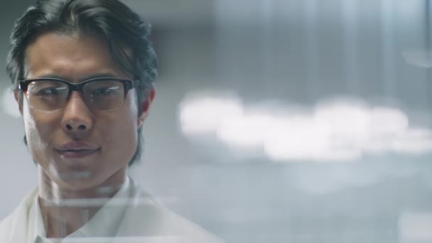 Laboratuvarda durup kameraya bakan kendine güvenen Asyalı bilim adamının cam duvarından çekilmiş bir portre. - Video, Çekim