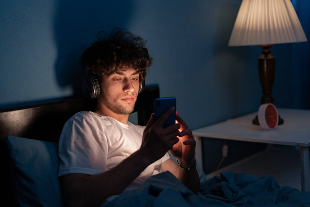 mobile εξαρτημένος άνθρωπος χρησιμοποιώντας smartphone περιήγηση στο διαδίκτυο για να παρακολουθήσουν ταινία ή να έχουν βιντεοκλήση σε απευθείας σύνδεση στο κρεβάτι δεν κοιμάται τη νύχτα. Αντιγραφή χώρου - Φωτογραφία, εικόνα