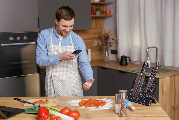 Bonito homem cozinhar na cozinha e fazer foto preparando comida em seu telefone móvel - Foto, Imagem