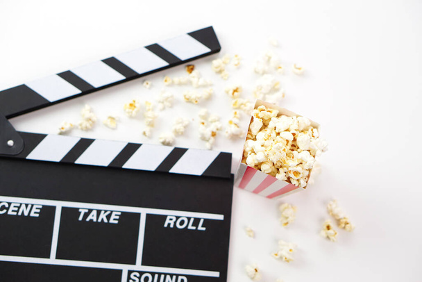 Focus of popcorn and blur clapperboard or movie slate black color on white background. Cinema industry, video production and film concept. - Photo, Image