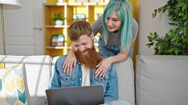 Man and woman couple sitting on sofa using laptop hugging at home - Photo, Image