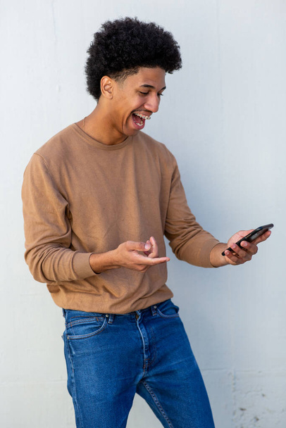 Glücklicher hispanischer Mann mit Telefon in der Hand vor weißem Hintergrund - Foto, Bild