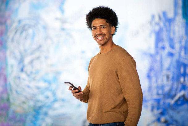 Retrato sorrindo jovem afro-americano de pé com telefone celular - Foto, Imagem
