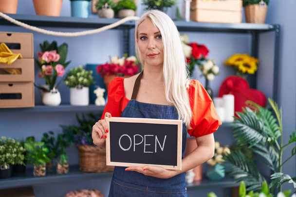 Caucasian woman working at florist holding open sign relaxed with serious expression on face. simple and natural looking at the camera.  - Photo, Image