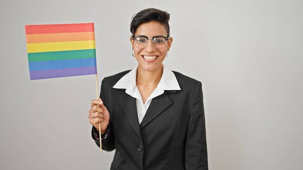 Junge schöne hispanische Geschäftsfrau lächelt selbstbewusst und hält Regenbogenfahne über isoliertem weißem Hintergrund - Foto, Bild