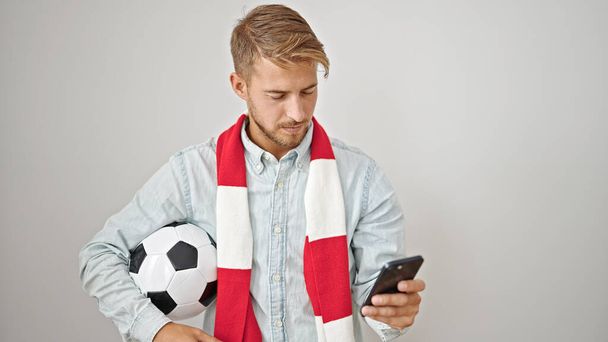 Jonge Kaukasische man ondersteunen voetbal team met behulp van smartphone over geïsoleerde witte achtergrond - Foto, afbeelding