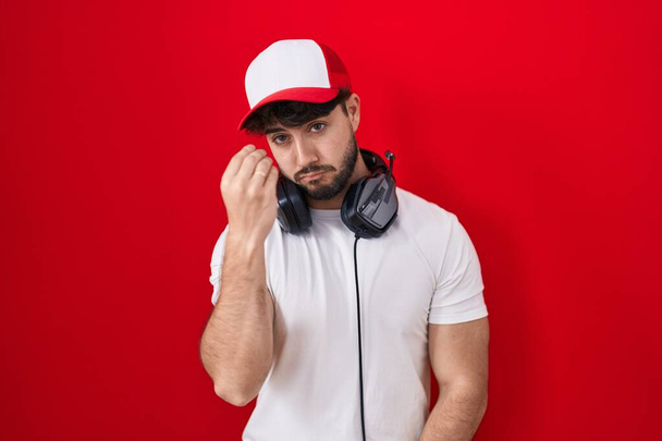 Hispanic man with beard wearing gamer hat and headphones doing italian gesture with hand and fingers confident expression  - Photo, Image