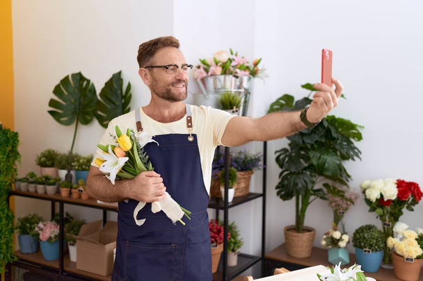 Middle age man florist make selfie by smartphone holding flowers at flower shop - Photo, Image