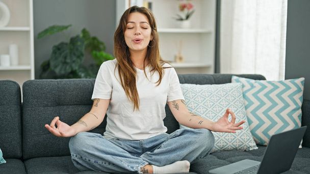 Mladá krásná hispánská žena dělá online jóga cvičení sedí na pohovce doma - Fotografie, Obrázek