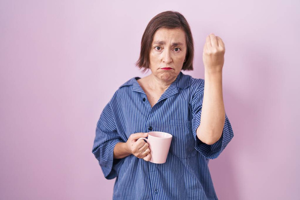 Latynoska kobieta w średnim wieku pije filiżankę kawy wykonując włoski gest z ręką i palcami  - Zdjęcie, obraz