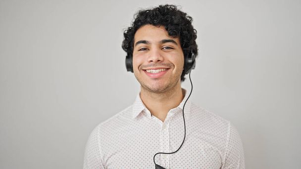 若いラテン人男性ビジネスワーカーは,孤立した白い背景の上にヘッドフォンを着用して自信を持って微笑みます - 写真・画像