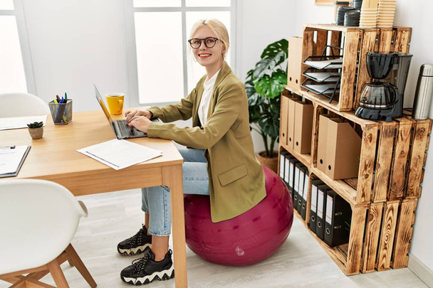 Jeune femme blonde travailleur d'affaires en utilisant un ordinateur portable assis sur balle en forme au bureau - Photo, image