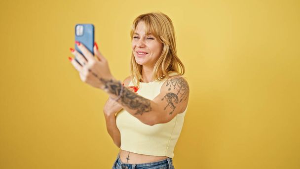 Nuori blondi nainen hymyilee luottavainen ottaa video puhelun yli eristetty keltainen tausta - Valokuva, kuva