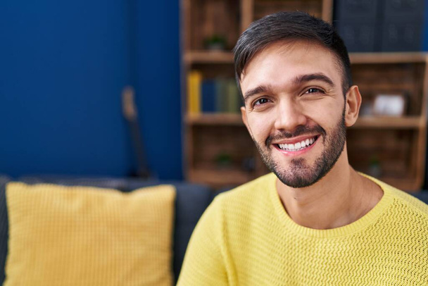 Jovem hispânico sorrindo confiante sentado no sofá em casa - Foto, Imagem