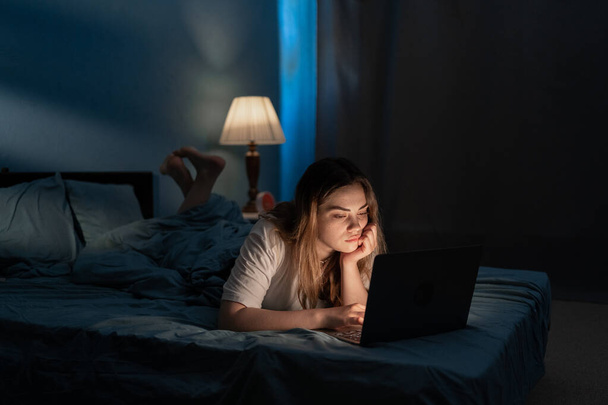 Fiatal nő pihen az ágyban laptoppal éjszaka. Fénymásolási hely - Fotó, kép