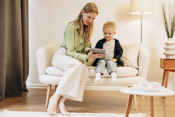 Woman sitting with her son and using tablet playing games - Foto, afbeelding