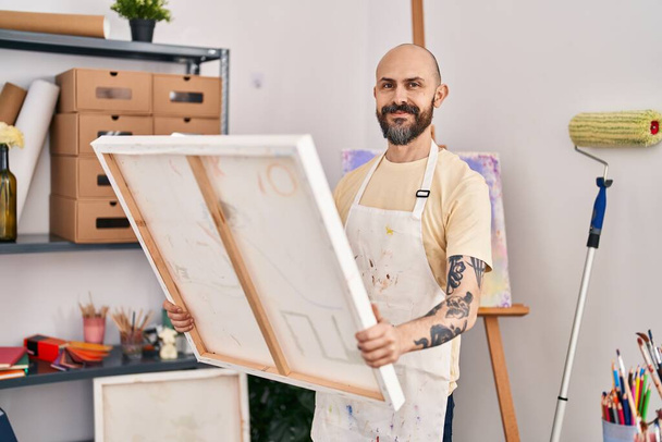 Νεαρός φαλακρός άνδρας καλλιτέχνης χαμογελά αυτοπεποίθηση αναζητούν κλήρωση στο στούντιο τέχνης - Φωτογραφία, εικόνα