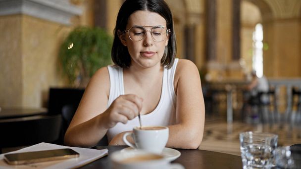 カフェテリアのテーブルに座ってコーヒーを飲む若い美しいヒスパニックの女性 - 写真・画像