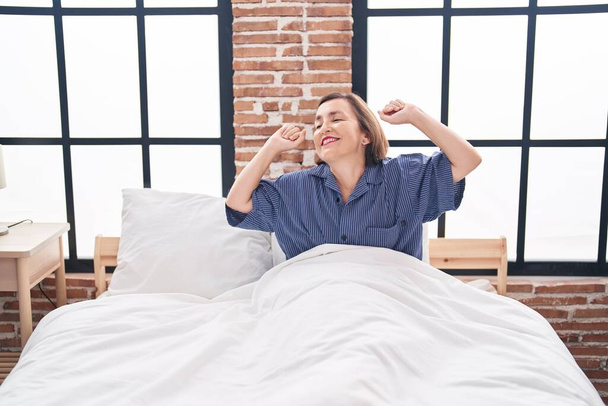 Middle age woman waking up stretching arms at bedroom - Photo, Image
