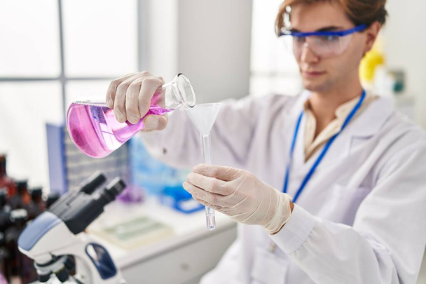 若い白人男性科学者が実験室で試験管に液体を注ぐ - 写真・画像