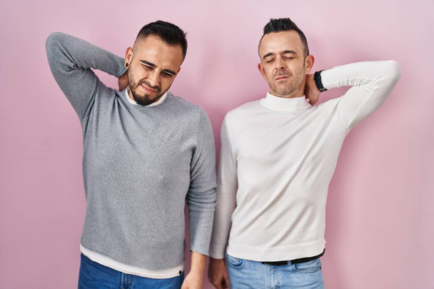 Homosexuelles Paar, das vor rosa Hintergrund steht, leidet unter Nackenschmerzen, Berührung des Nackens mit der Hand, Muskelschmerzen  - Foto, Bild