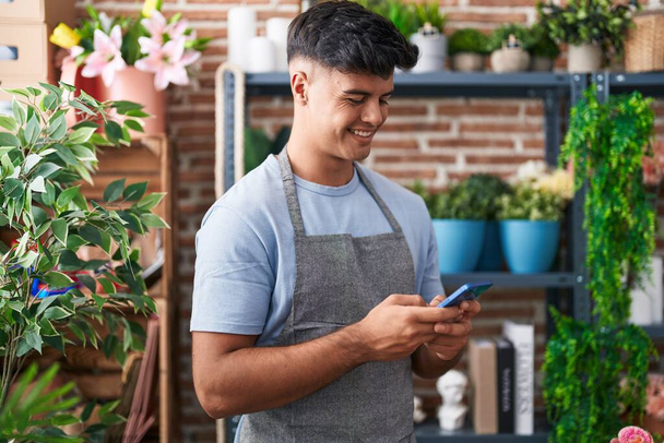 Young hispanic man florist smiling confident using smartphone at flower shop - 写真・画像